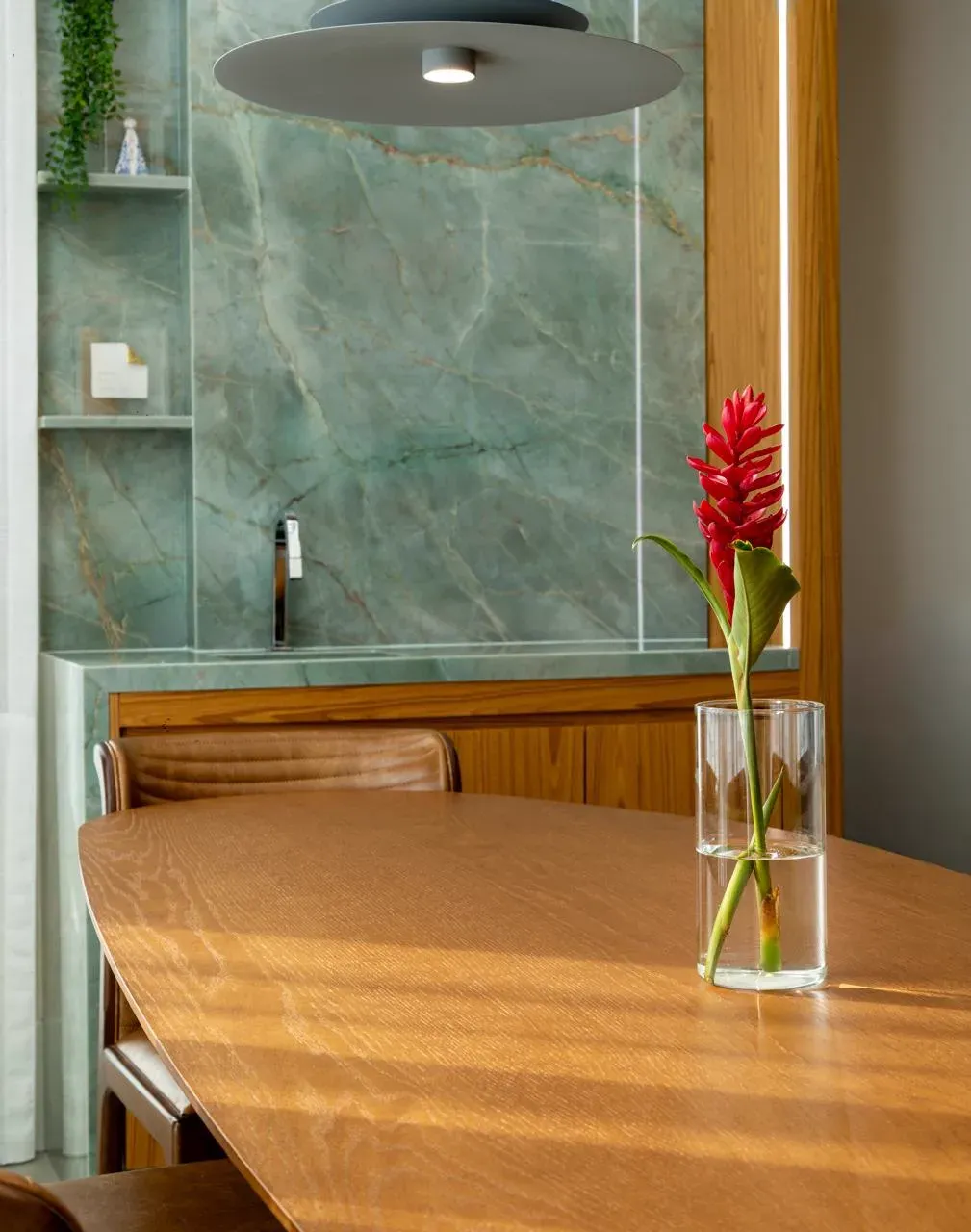 Detalhe do painel de quartzito verde com mesa de madeira e flor tropical