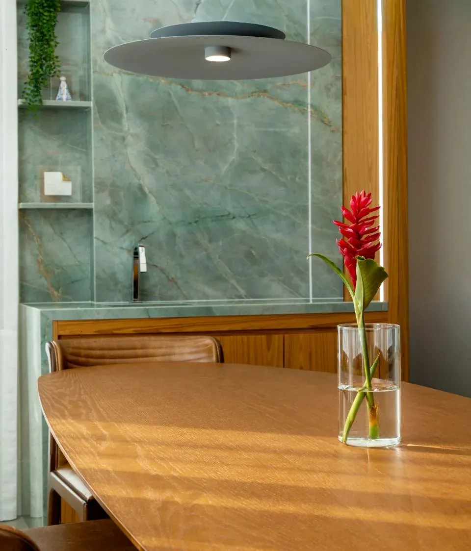 Sala de jantar com painel de quartzito verde, marcenaria em madeira clara, mesa oval e luminária de disco